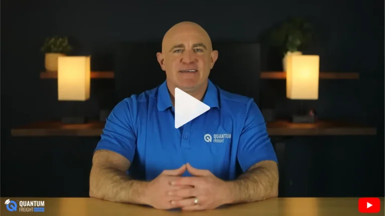 Video thumbnail: a bald man in a blue polo speaks to the camera at a desk, warm lamps in the background, play button center stage, Quantum Freight logo visible.